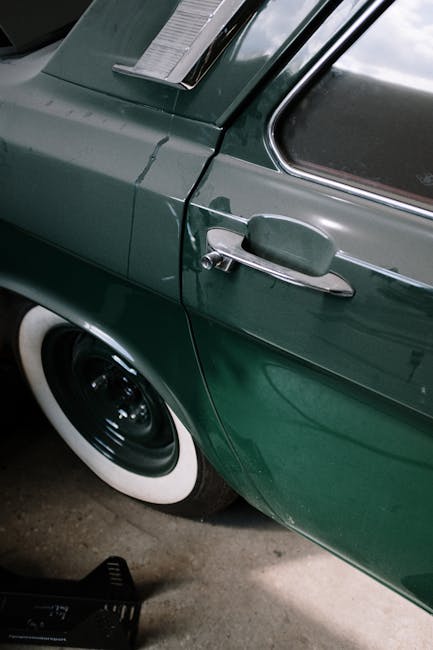 Close-up of a vintage green car with a whitewall tire and chrome details in a garage setting.